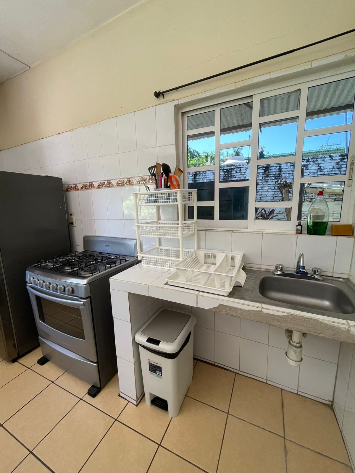 A kitchen with a gas stove, oven, white tiled backsplash, window with view, and a sink.