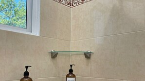 A bathroom with beige tiles, a showerhead, and two shelves holding bottles of body wash. - Serene 3-bedroom apartment with AC in Puerto Escondido (Puerto Escondido)