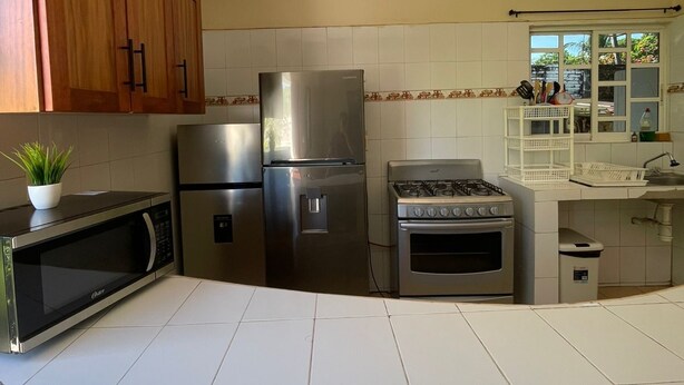 A kitchen with wooden cabinets, a stainless steel refrigerator, a microwave, a gas stove, and a tiled backsplash. - Serene 3-bedroom apartment with AC in Puerto Escondido (Puerto Escondido)