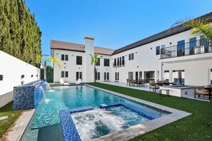 Un espace piscine moderne doté d’un jacuzzi, entouré d’une pelouse bien entretenue et d’un bâtiment blanc avec de nombreuses fenêtres et des balcons.