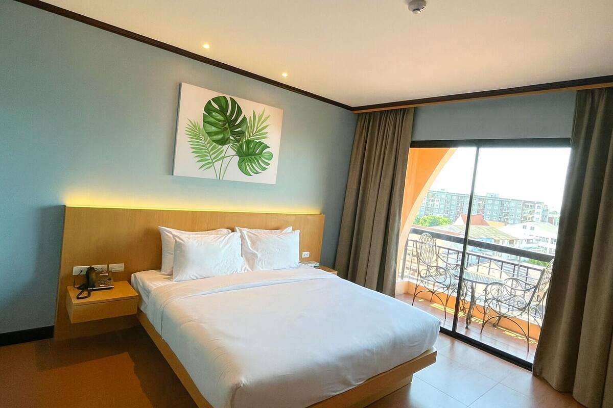 A hotel room with a large bed, a nightstand, a telephone, and a view of the city through a balcony.
