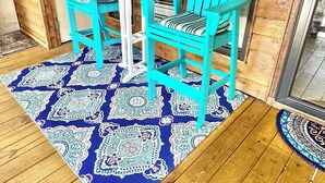 Interior em madeira com uma mesa e duas cadeiras, um tapete estampado e uma porta com uma placa.