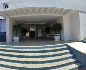 A building entrance with a set of stairs leading up to a door, potted plants, and a sign with the letter 'A'.
