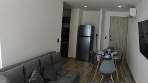 A compact living space with a grey sofa, a dining table with chairs, a refrigerator, and a wooden door. - Beautiful apartment in Residencial Astorias! (Acapulco de Juárez)