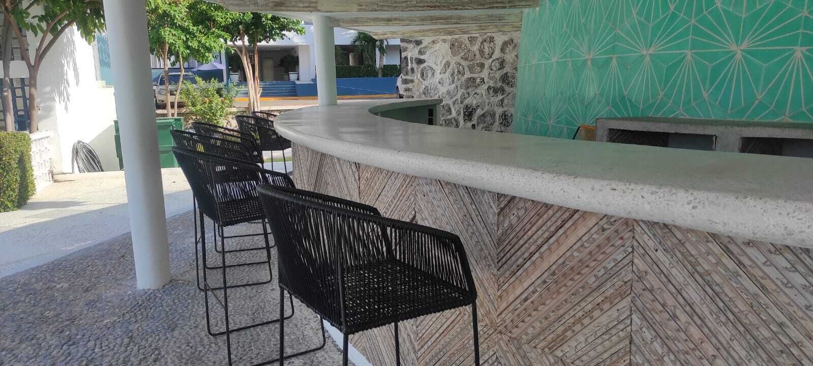 A bar area with a stone wall and a green patterned wall. There are black chairs and a white counter.