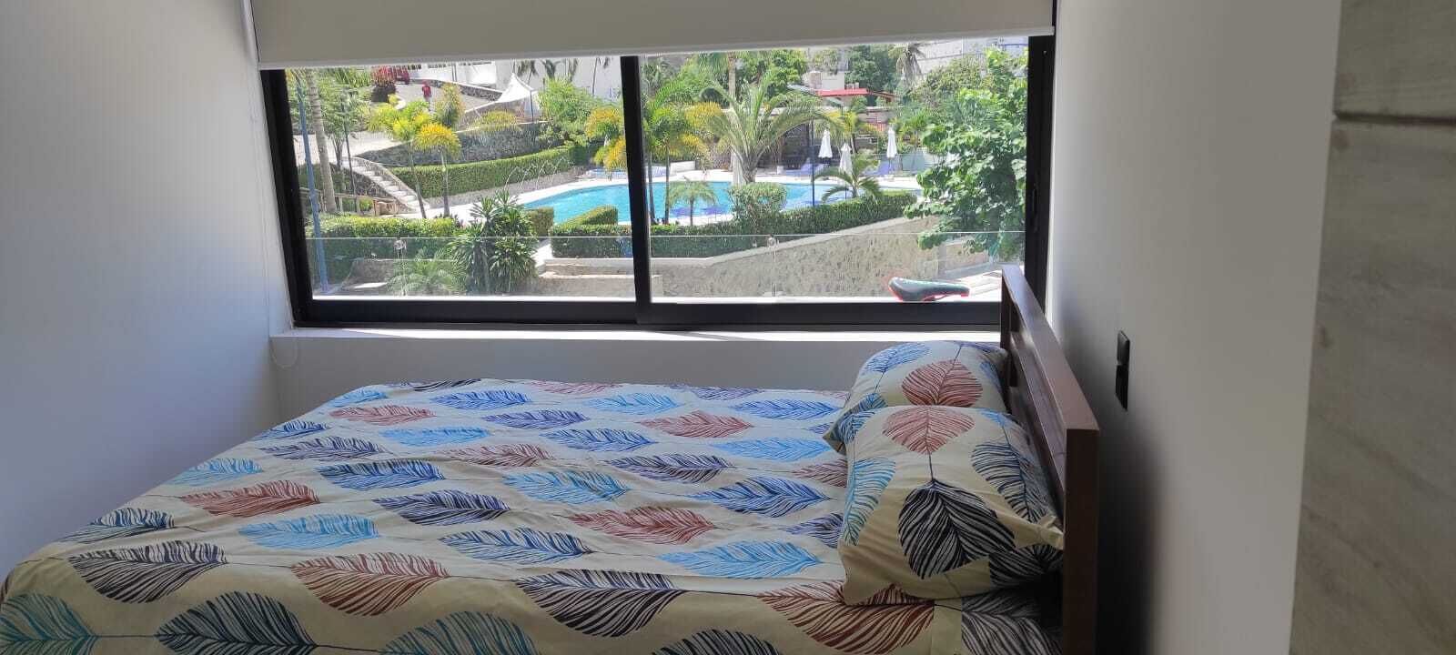 A bedroom with a bed, a window, and a view of a swimming pool and greenery.