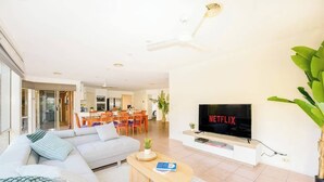Een moderne woonkamer met een grote flatscreen-tv, een bank, een salontafel en een eethoek op de achtergrond.