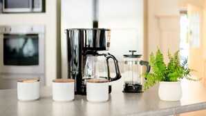 Een keuken met een koffiezetapparaat, een blender en een bloempot op het aanrecht.