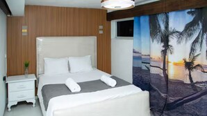 A hotel room with a large bed, a nightstand, and a wall mural of a beach scene. - Enjoyable 1-bedroom apartment with AC in vibrant Sosúa (Sosúa)