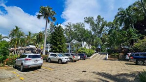 A parking lot with several cars, surrounded by lush greenery and palm trees. - Enjoyable 1-bedroom apartment with AC in vibrant Sosúa (Sosúa)