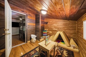 Quarto aconchegante com paredes e chão de madeira, uma cama, uma mesa com ábaco e uma tenda de brincadeira.