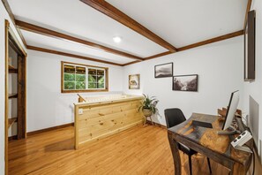 Quarto com escrivaninha de madeira, uma cadeira, uma janela e teto com vigas aparentes.