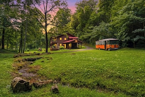 A cabin with a porch, a small deck, and a bus parked in a forested area. - Private 1-Acre Gatlinburg Cabin / Hot Tub, Theater & Game Room (Gatlinburg)