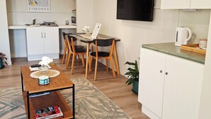 Een knus woongedeelte met een eethoek, kitchenette en een aan de muur bevestigde televisie.