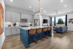 A modern kitchen with grey cabinets, a central island with bar stools, a stainless steel refrigerator, and a flat-screen TV mounted on the wall. - Lux Nashville Home w/ Pool Table & Rooftop FirePit (Nashville)