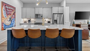 Une cuisine moderne dotée d’un îlot central, de tabourets de bar, d’appareils électroménagers en acier inoxydable et d’un néon.