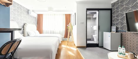 Habitación de hotel con dos camas, un escritorio, una silla, un televisor y una pequeña mesa con botellas de agua.