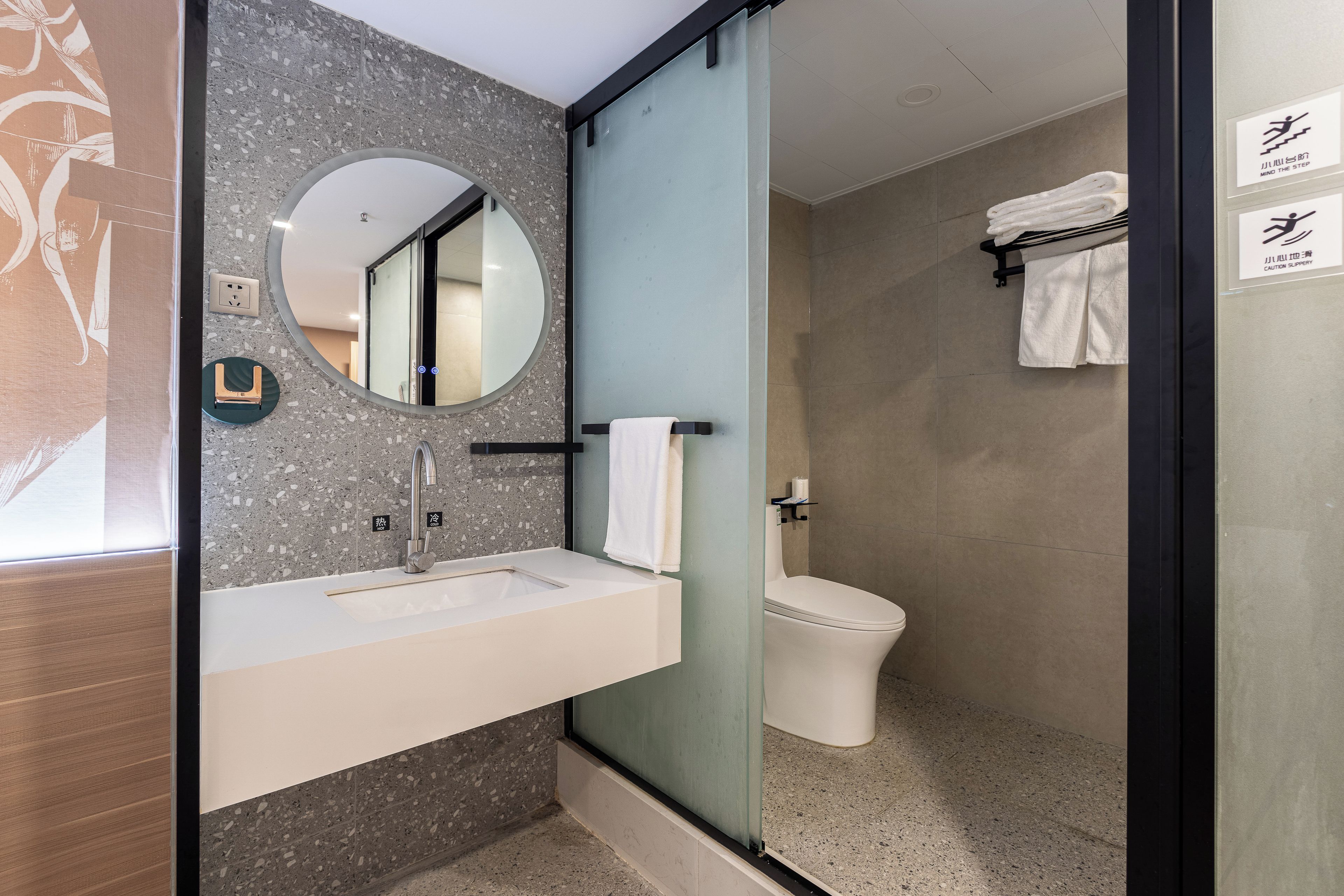 A modern bathroom with a granite countertop sink, a round mirror, and a toilet.