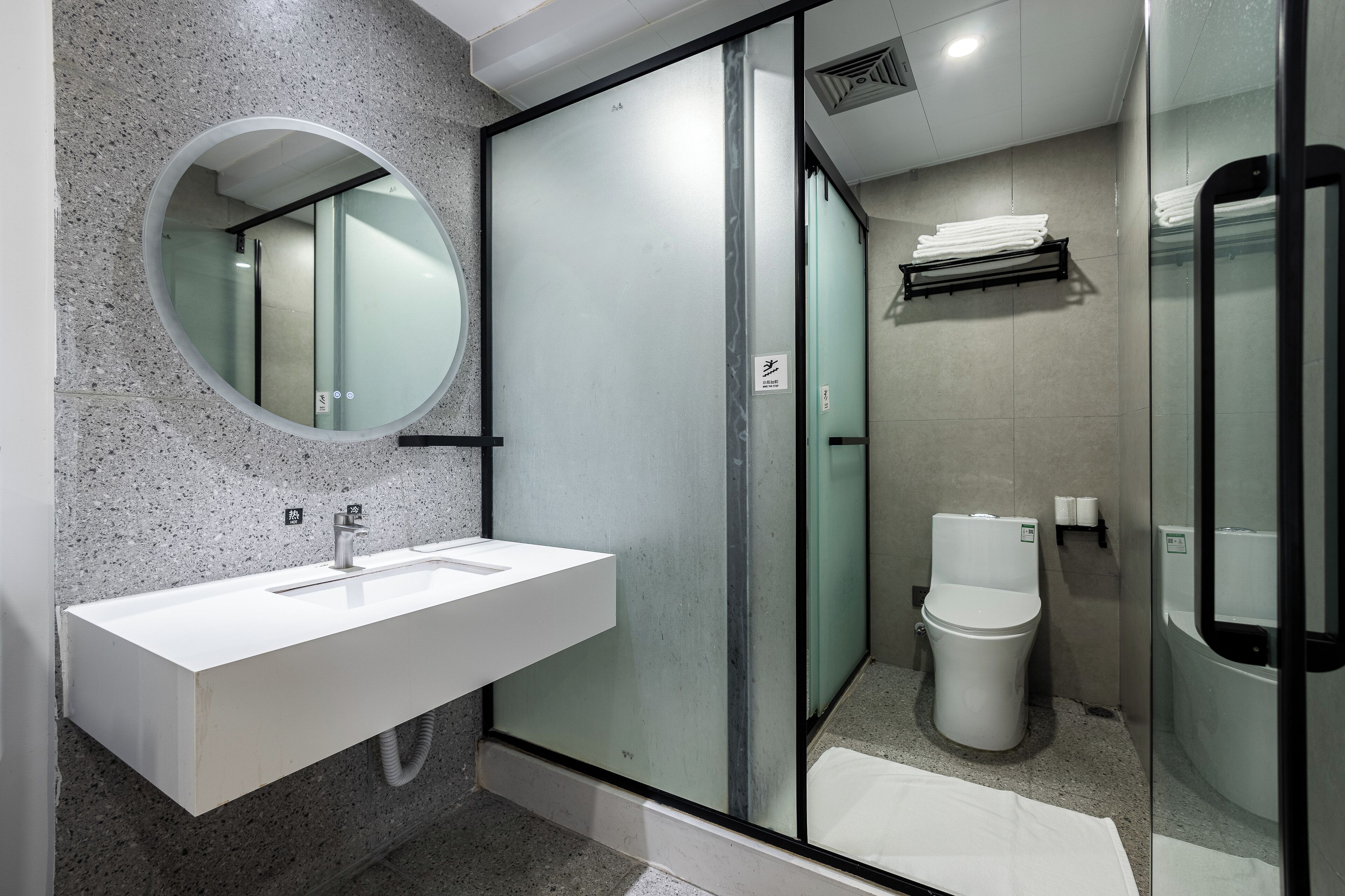 Een moderne badkamer met een wit wastafel, een ronde spiegel, een douchecabine van glas en een toilet.