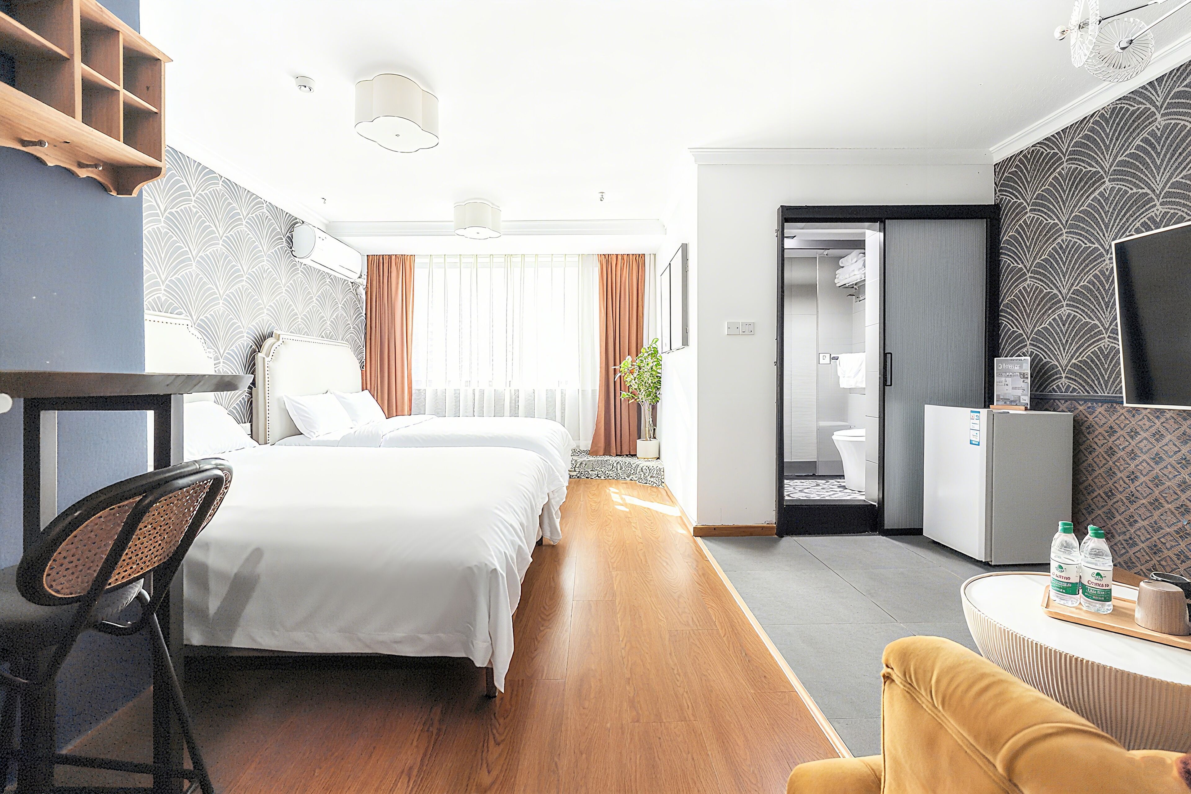 A hotel room with a bed, a desk, a chair, a small table with bottles, and a television.