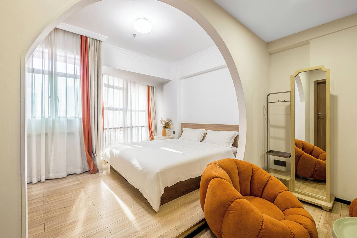 A hotel room with a large bed, a mirror, and an orange chair.