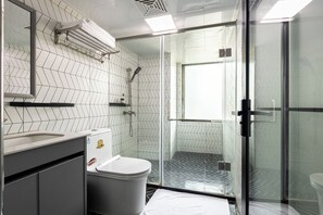 Egy modern fürőszoba fehér és fekete színű, halszálkamintás csempével, üveg zuhanykabinnal és fehér fedéllel ellátott WC-vel.