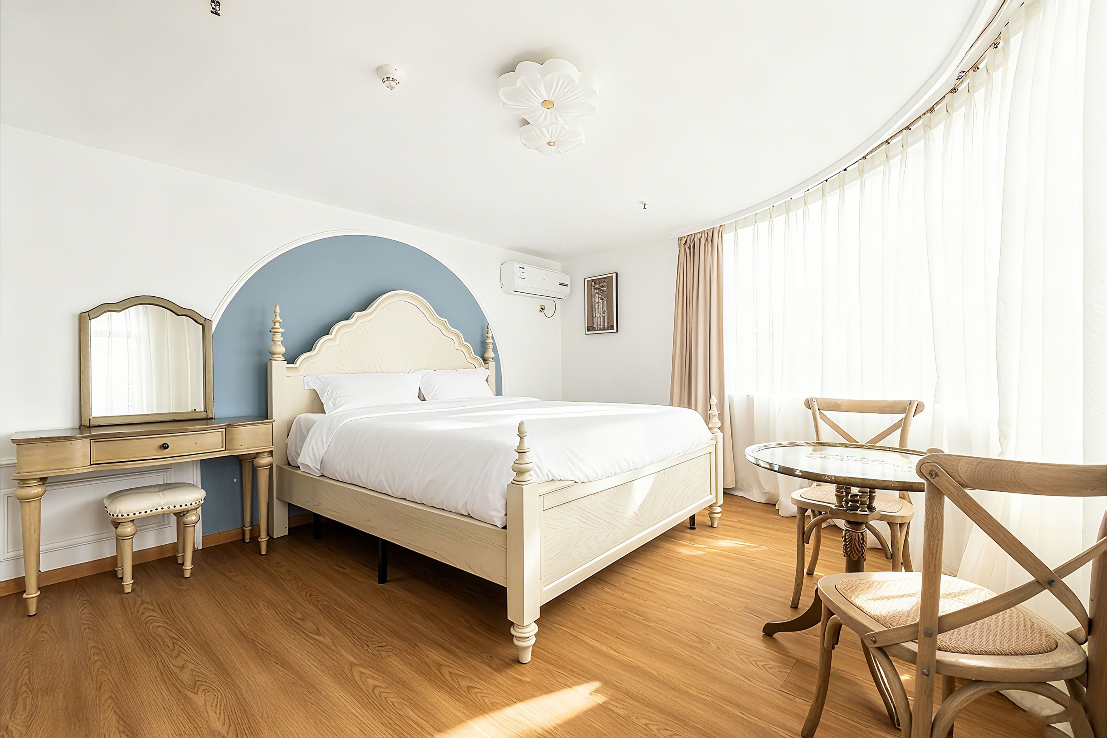 A bedroom with a bed, a vanity with a mirror, a chair, and a small table.