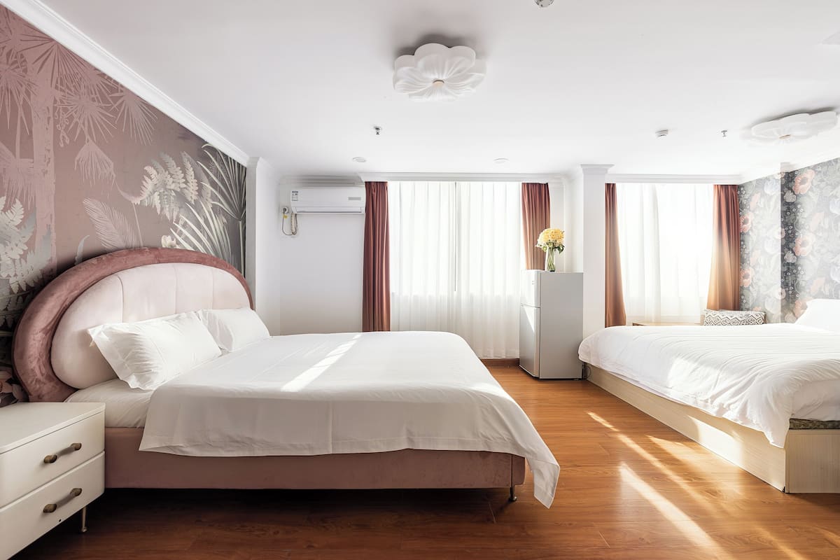 A hotel room with a large bed, a bedside table, a nightstand, a dresser, and a wall-mounted air conditioner.