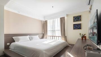 A hotel room with a large bed, a wooden headboard, a desk with a chair, a flat-screen TV, and two framed artworks on the wall.