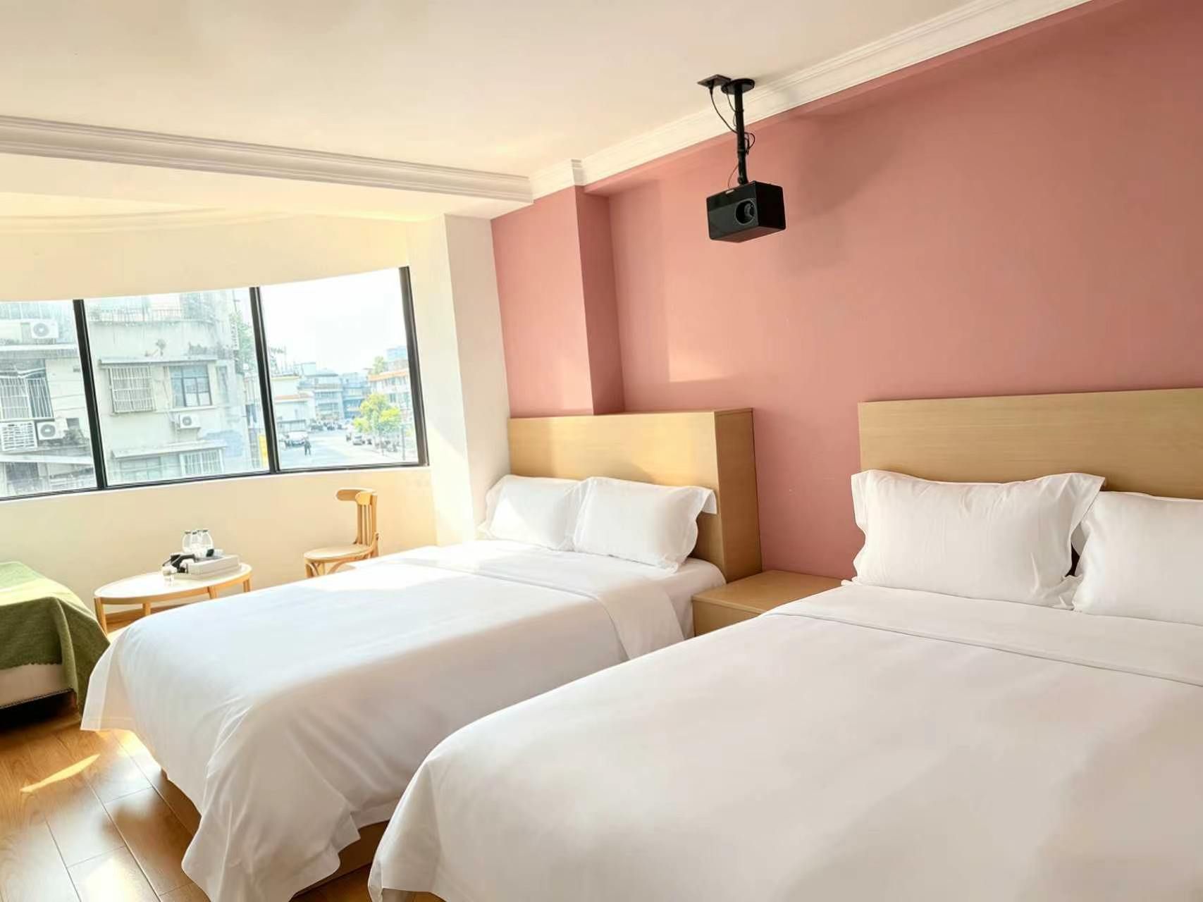 Ein Hotelzimmer mit zwei Betten, einem kleinen Tisch, einem Stuhl und einem an der Wand montierten Projektor.