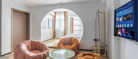 Ein modernes Hotelzimmer mit großem Fernseher, bequemen Sitzmöglichkeiten, einem Bett und Blick auf die Stadt.