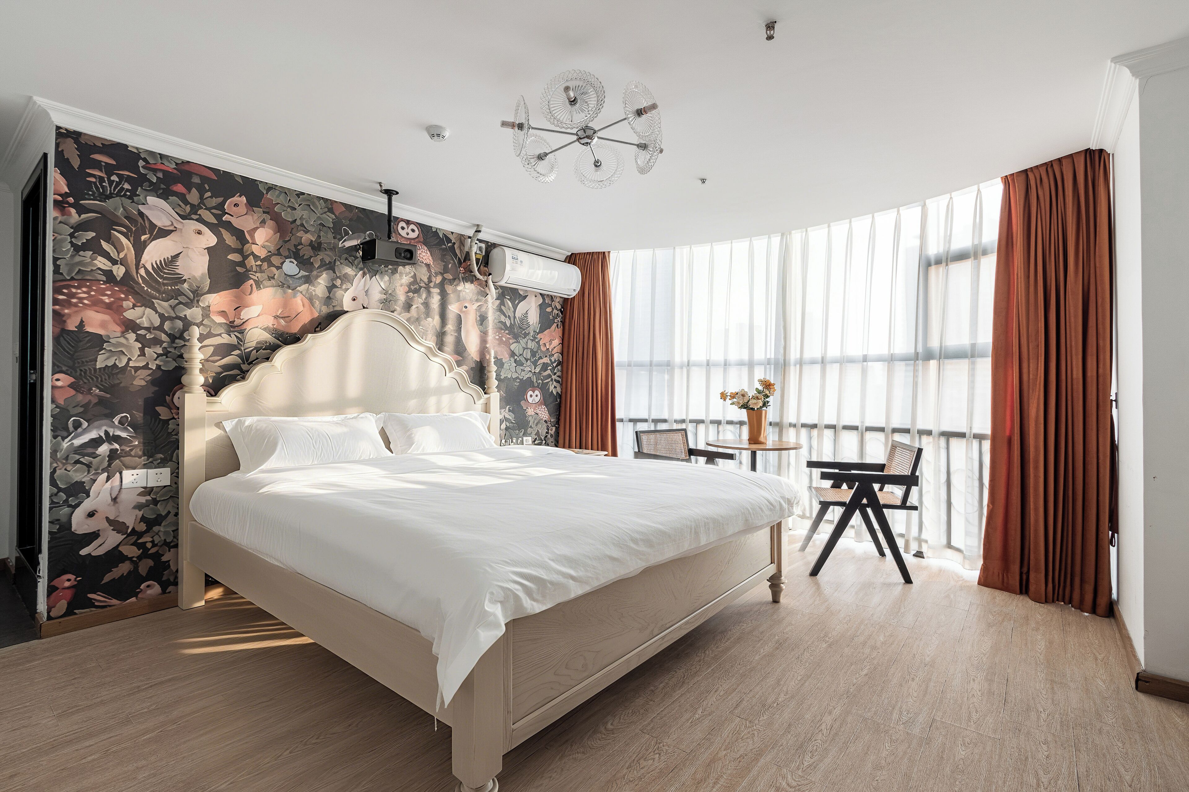 Een slaapkamer met een groot bed, een muurschildering, een plafondventilator en uitzicht op de omgeving.
