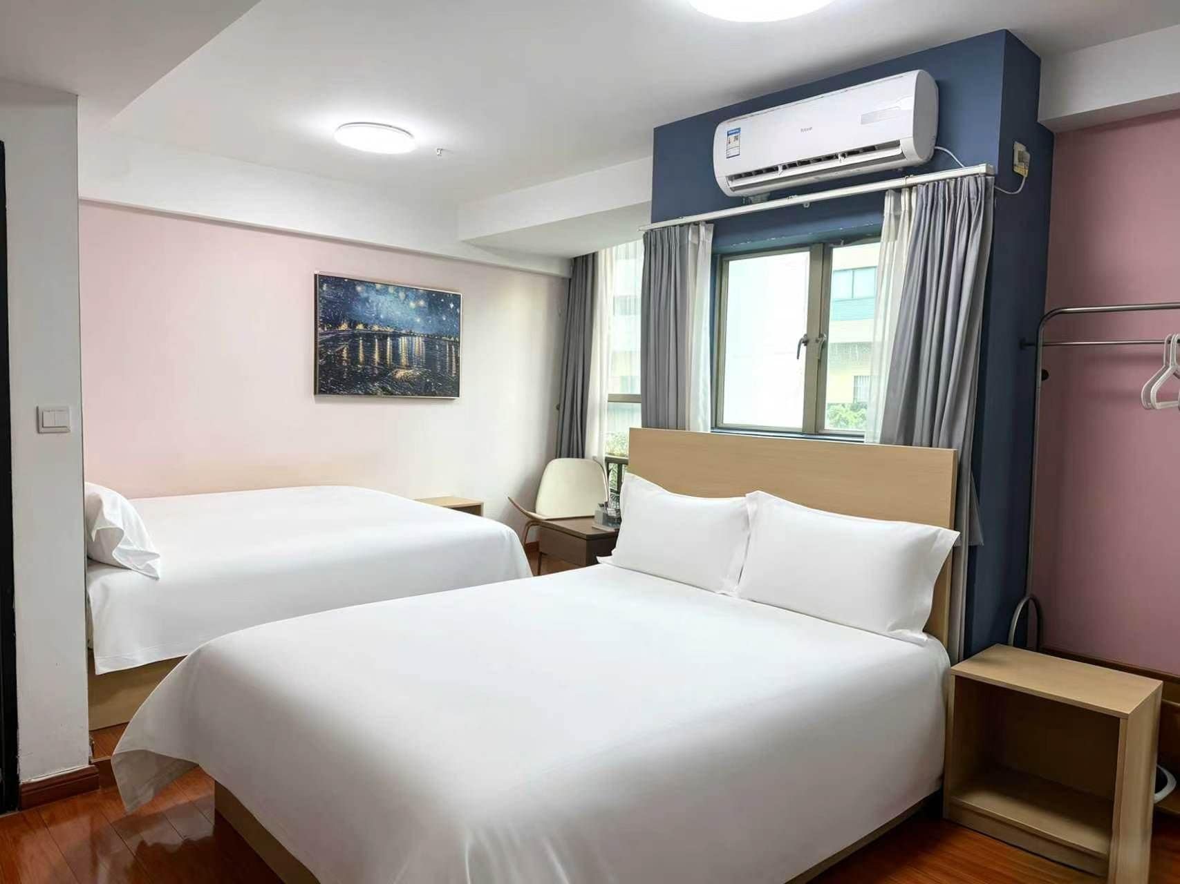 Una camera d'albergo con due letti, un climatizzatore, un quadro raffigurante il cielo notturno e una finestra con tende.