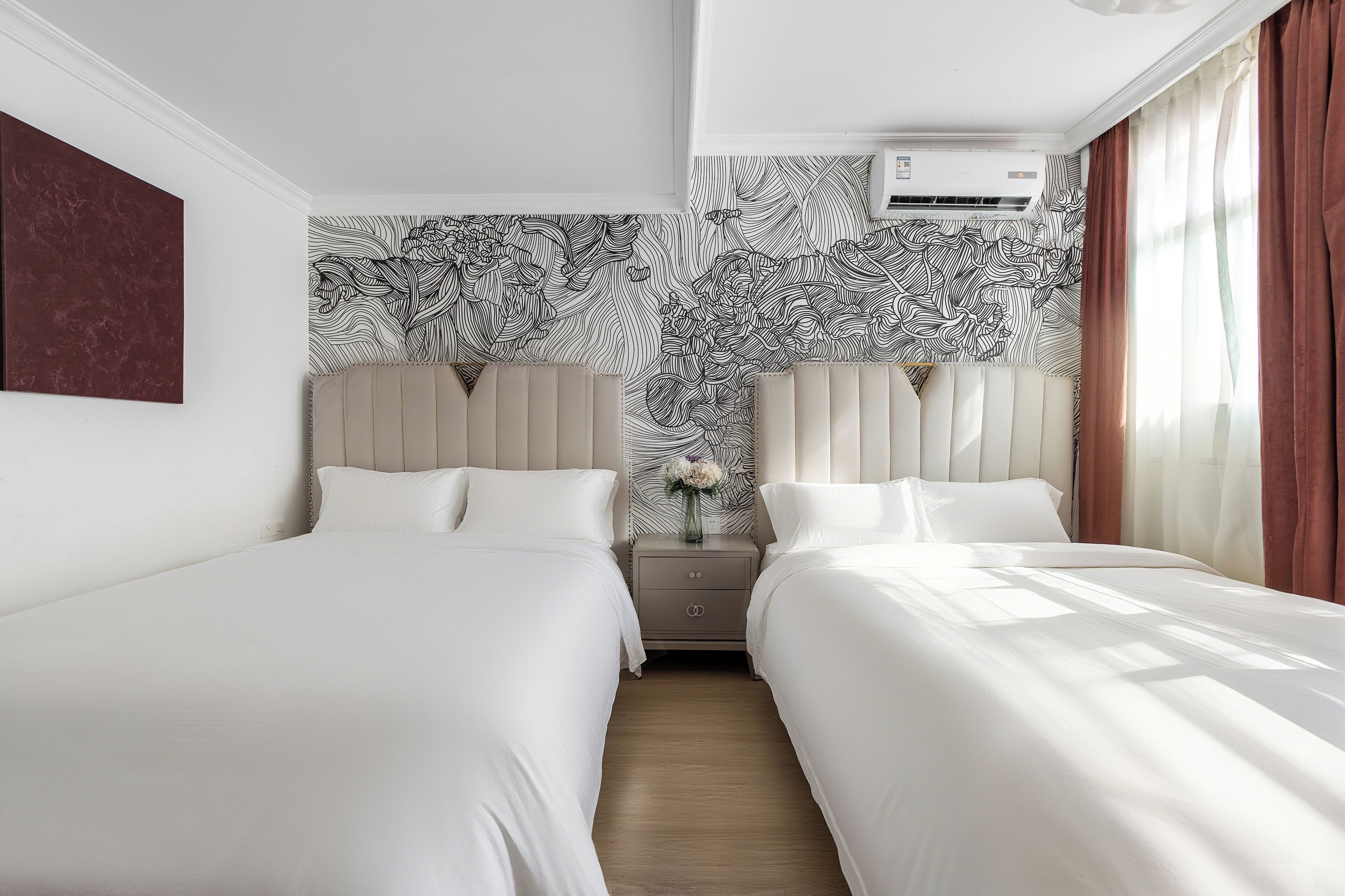 A hotel room with two beds, a nightstand with a vase of flowers, and a patterned wallpaper.