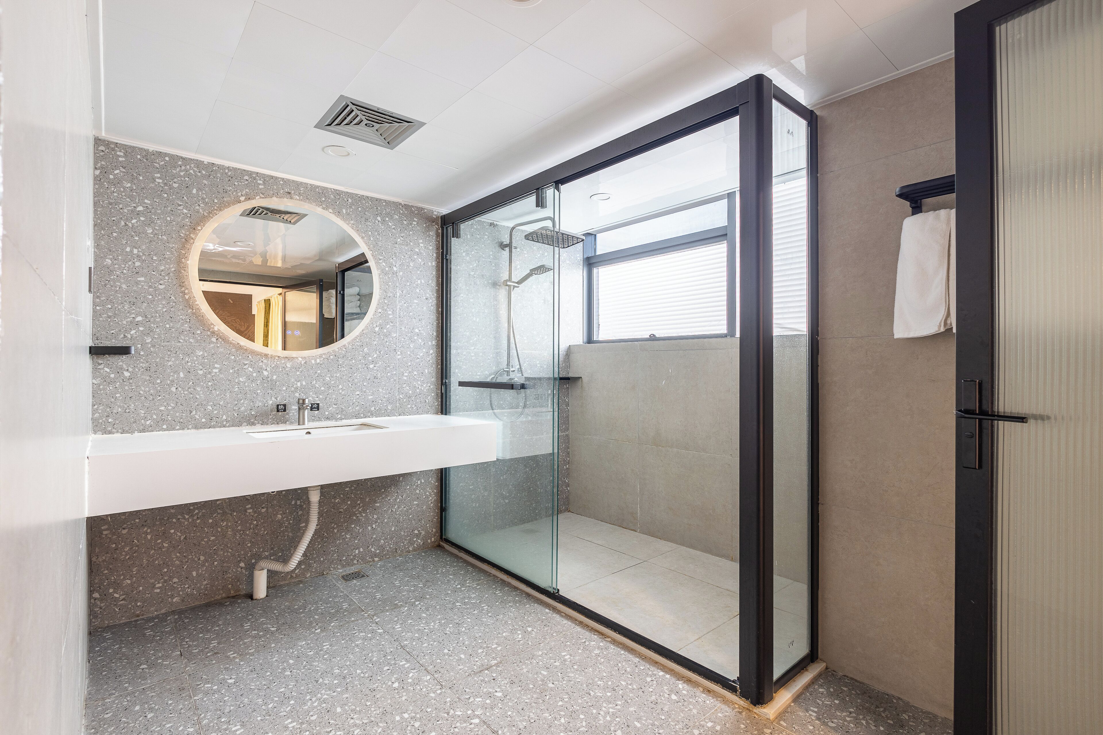 A modern bathroom with a glass-enclosed shower, a round mirror, and a white sink.