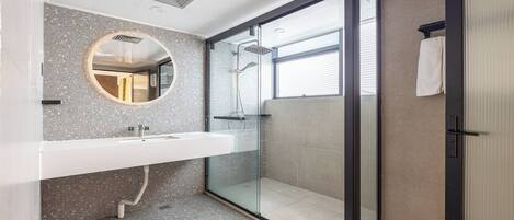 A modern bathroom with a glass-enclosed shower, a round mirror, and a white sink.