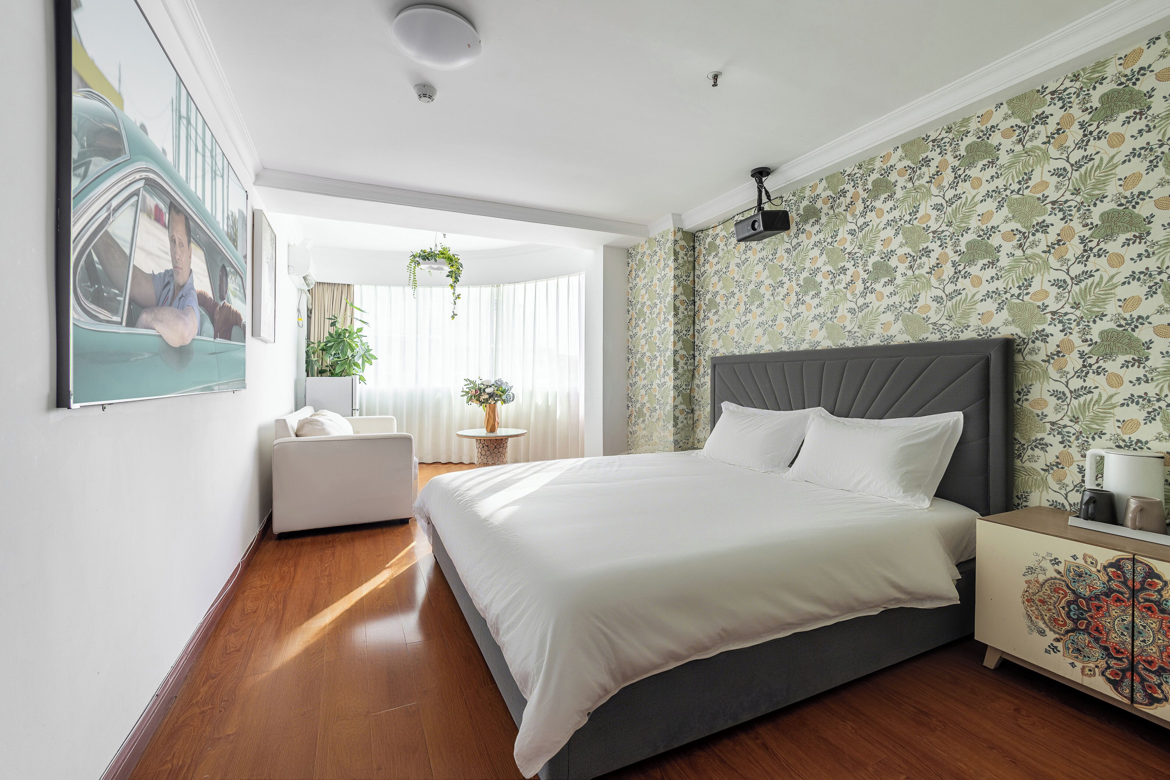 A modern bedroom with a large bed, a white sofa, a small table with a plant, and a decorative cabinet.