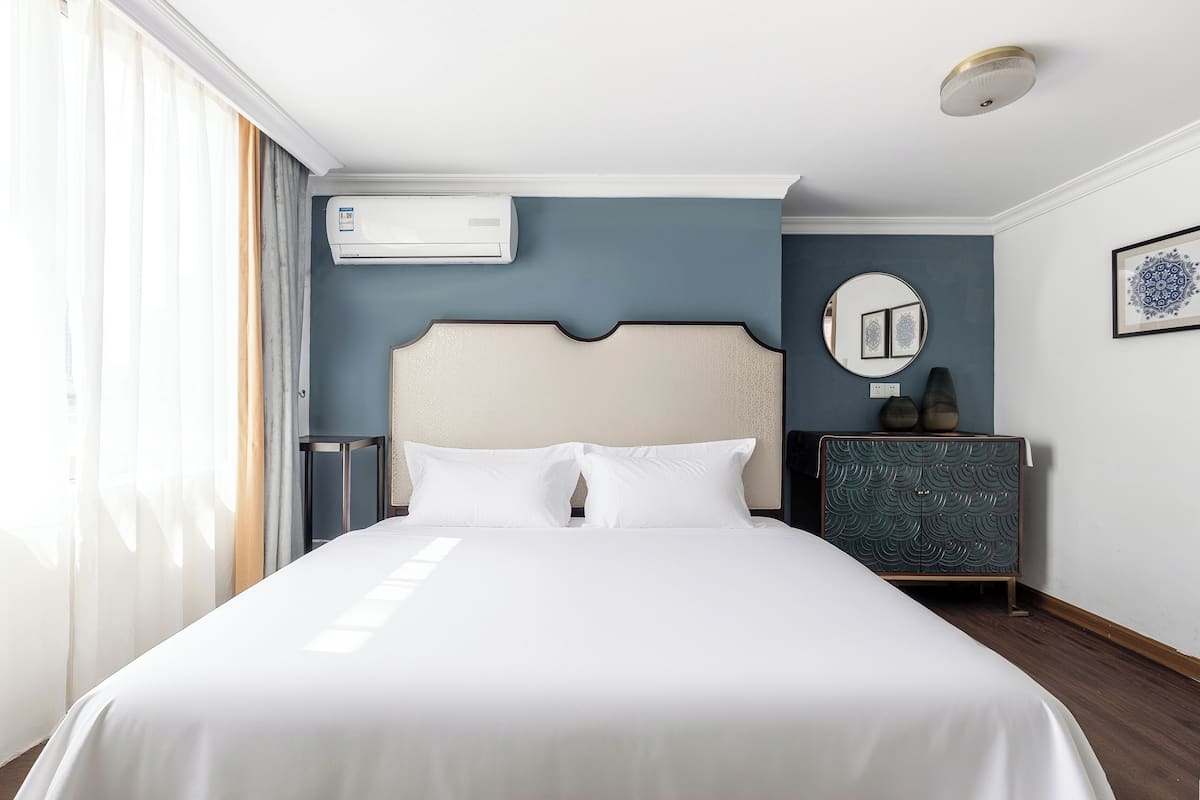 A hotel room with a large bed, a dresser, a mirror, and an air conditioning unit on the wall.