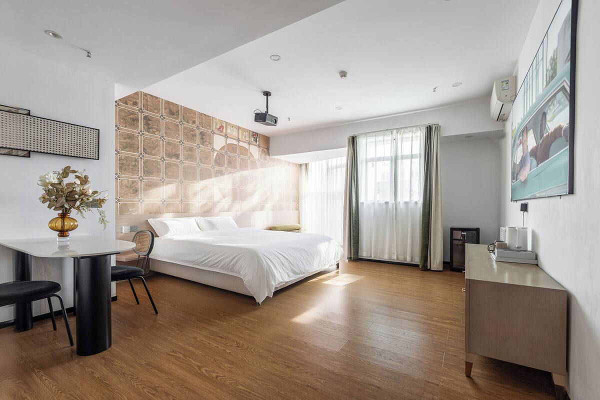 A modern hotel room with a bed, a desk, and a small kitchenette.