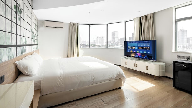 Una habitación de hotel moderna con una cama grande, un televisor de pantalla plana, vistas a la ciudad y un ventanal amplio.