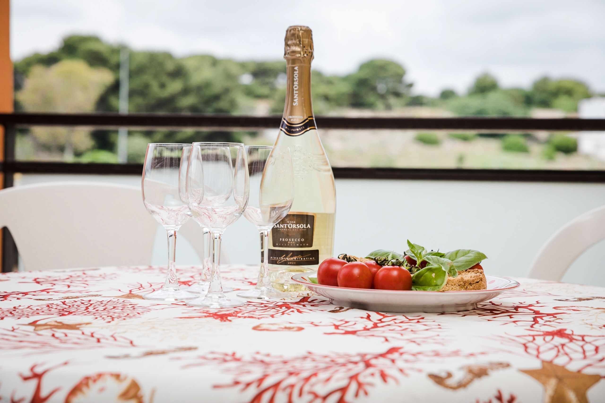 A table with a bottle of Santorini wine, two glasses, and a plate with tomatoes and basil.