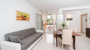 Een moderne woonkamer met een grijze bank, een eettafel met stoelen en een schilderij aan de muur.