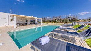 Un'area piscina moderna con lettini e una zona relax coperta.