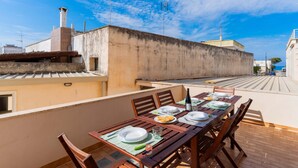 Un área de comedor al aire libre con una mesa dispuesta para dos personas, vistas del paisaje urbano y un cielo despejado.