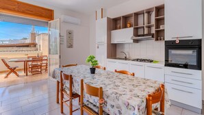 Una cocina moderna con armarios blancos, una mesa de comedor con mantel floral y vistas de la ciudad a través de un ventanal grande.