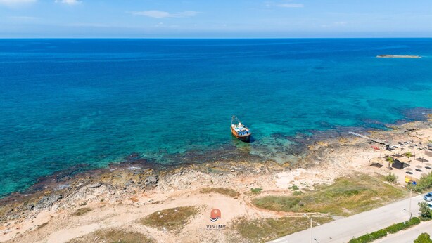 Vista aérea de una zona costera con aguas azul turquesa, un barco anclado cerca de la orilla y una playa pequeña con edificaciones.