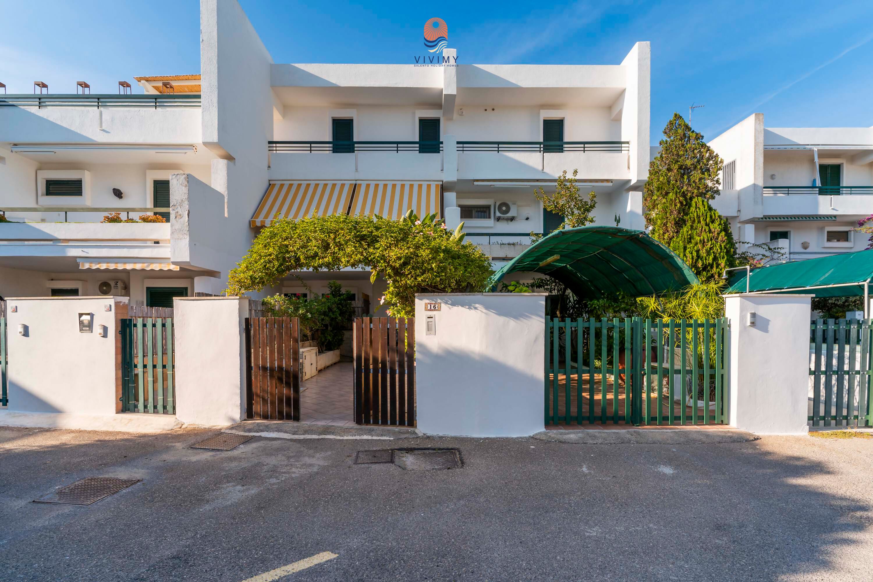 A modern multi-story building with a gated entrance, balconies, and a clear sky.