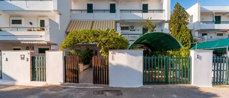 A modern multi-story building with a gated entrance, balconies, and a clear sky.