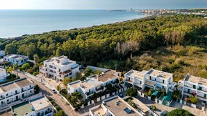 Una zona residenziale costiera con edifici moderni bianchi, vista sul mare e vegetazione lussureggiante.