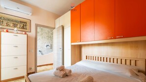 Una camera da letto con un letto, una testata in legno, un armadio con ante arancioni, una cassettiera bianca e un condizionatore d'aria a parete.